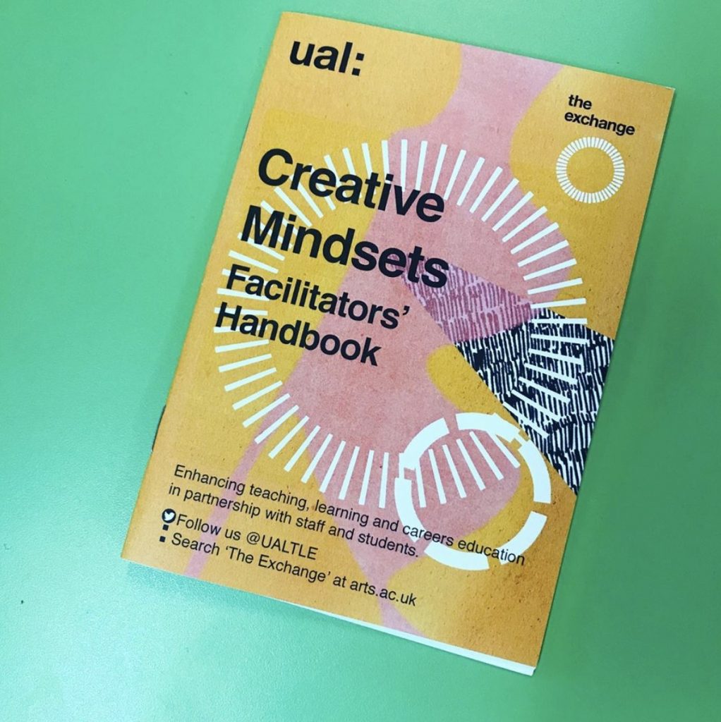 Image of yellow and pink Creative Mindsets Facilitators Handbook on green surface