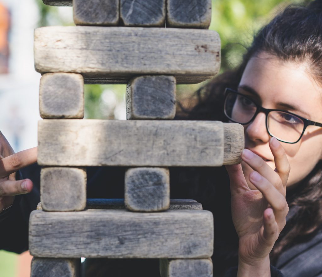 Close up of woman in glasses playing "jenga" game with giant wooden blocks
