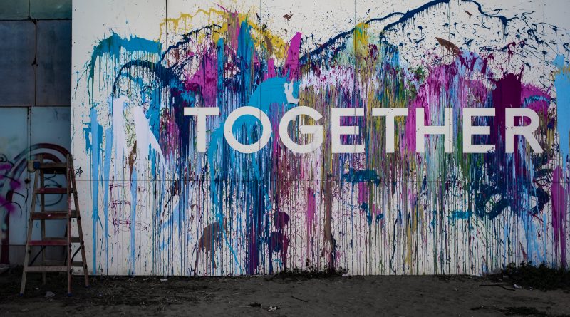 A wall with the word Together painted on it surrounded by multicolour paint splatters.